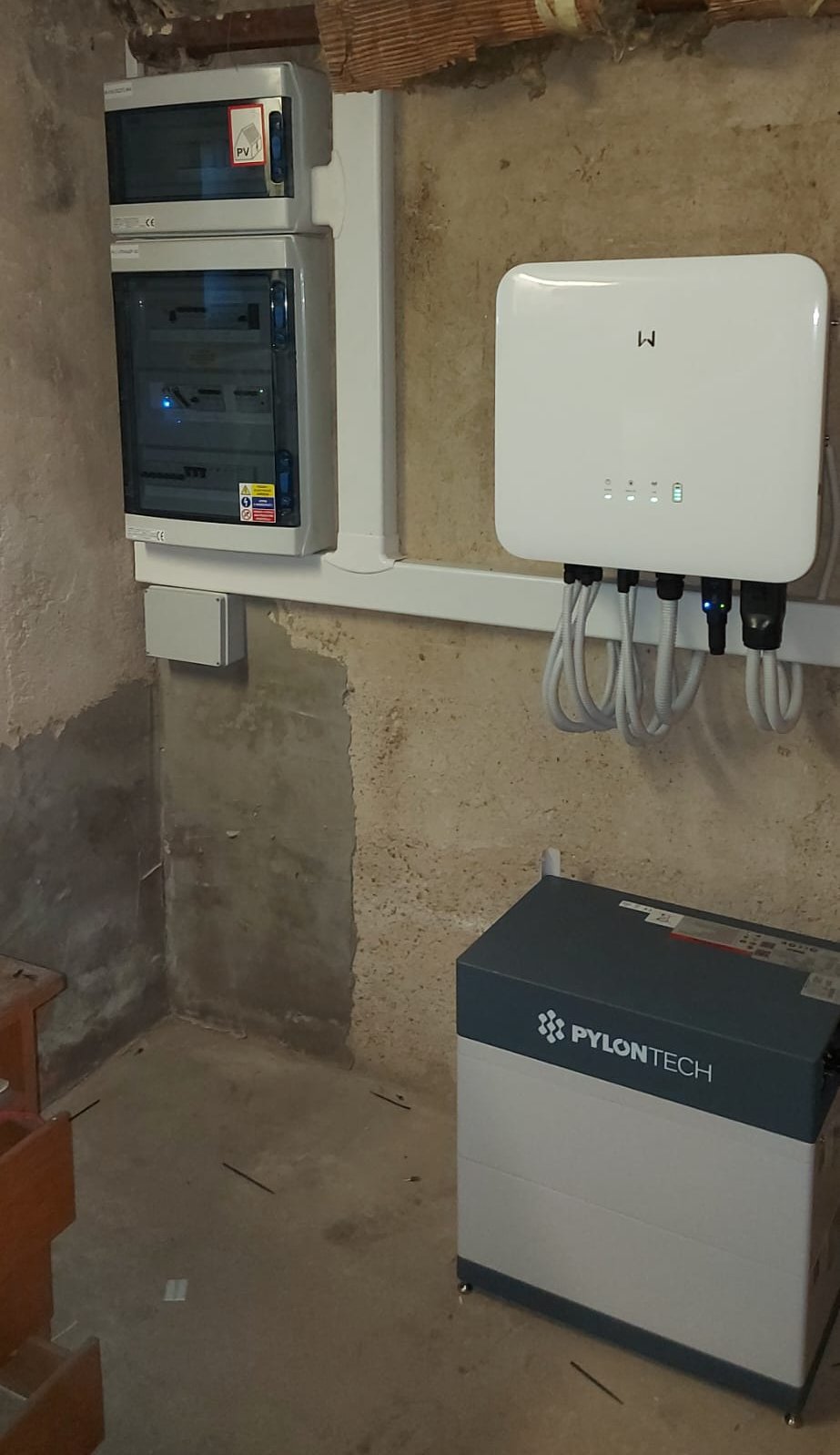 Střídač, dva rozvaděče a bateriový modul na betonové stěně sklepa